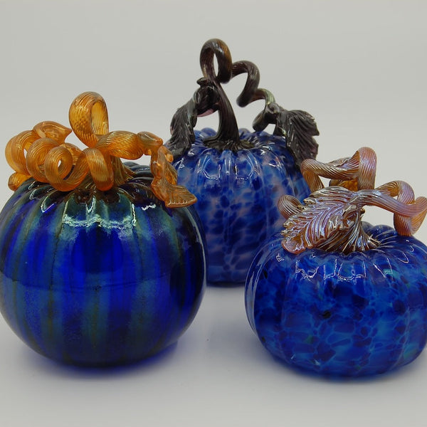 Three blue glass pumpkins with decorative stems on a white background