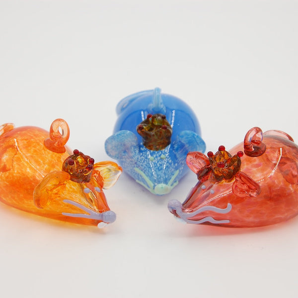 Three blown glass mice ornaments in orange, blue, and red on a white background
