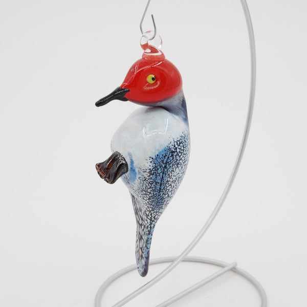 Glass ornament of a bird with a red head and blue body on a white background