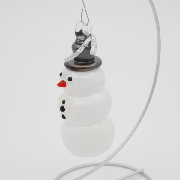 Snowman-shaped glass ornament with a black tophat on a white background